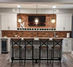 a kitchen with three bar stools in front of a brick wall and white cabinets