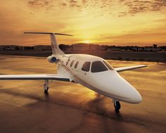 a small white plane sitting on top of an airport tarmac at sunset with the sun in the background