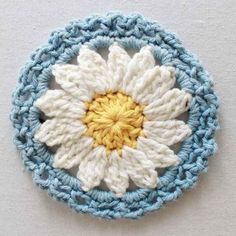 a crocheted white and blue flower with yellow center sits on top of a table