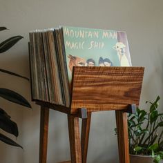 a stack of vinyl records sitting on top of a wooden stand next to a potted plant