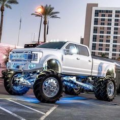 a large white truck parked in a parking lot next to tall buildings and palm trees