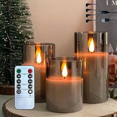 three lit candles sitting on top of a wooden table next to a remote control and christmas tree