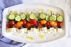 a white plate topped with cucumbers, tomatoes and olives on skewers