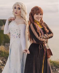 two women dressed in costumes standing next to each other on a hill near the ocean