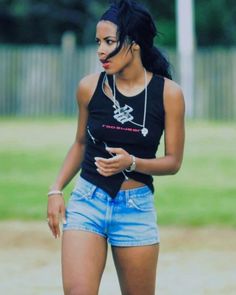 a woman in shorts and a black shirt is standing on the grass with her cell phone up to her ear