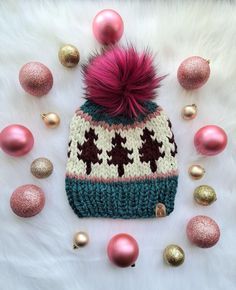 a knitted hat with pink and green pom - poms surrounded by christmas ornaments