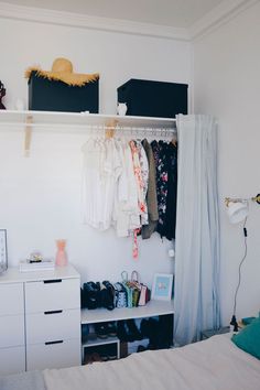 a bedroom with white walls and clothes hanging on the rack in it's corner