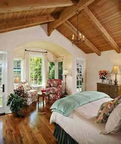 a bedroom with wood floors and white walls has a large bed, two chairs, and a chandelier hanging from the ceiling