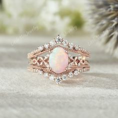 a white opal and diamond ring sitting on top of a table next to a pine tree