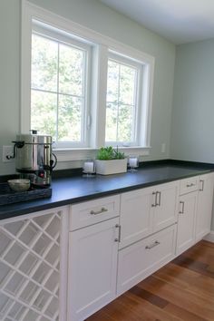 an empty kitchen with white cabinets and black counter tops is pictured in this image, there are two windows on the far wall