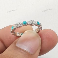 a person holding a ring in their left hand with diamonds and turquoise stones on it