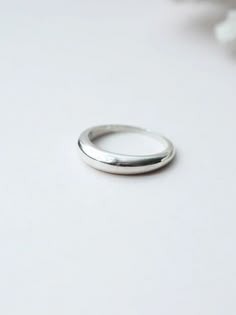 a thin silver ring sitting on top of a white table next to some pink flowers