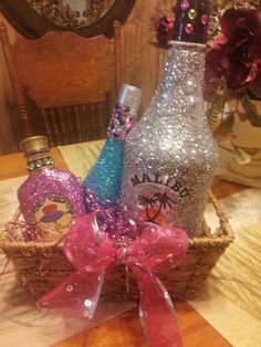 two bottles in a basket with pink bows on a table next to a mirror and vase