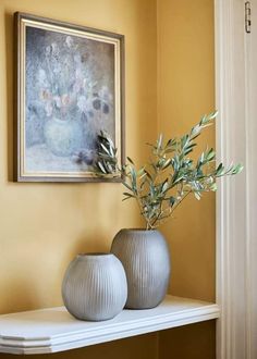 two vases with green plants sit on a shelf in front of a framed painting