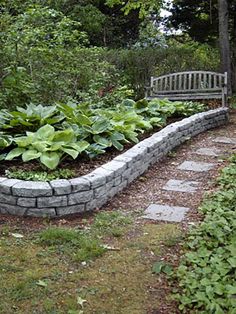 a stone garden bed with green plants in the middle and a bench on the other side