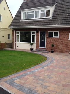 a brick driveway in front of a house with grass on the side and two large windows