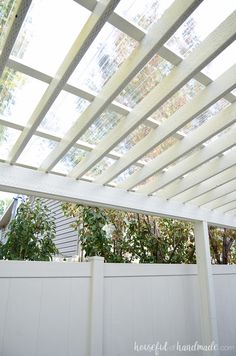 a white pergolated roof over a white fence with trees in the back ground