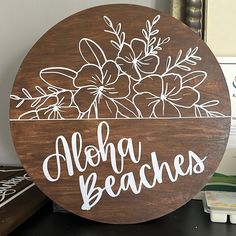 a wooden sign that says aloha beaches with flowers in the center on a table