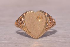 This stunning piece, known as The Classic Heart, features a beautifully engraved heart signet with a natural diamond accent. The ring is crafted in yellow gold, showcasing intricate filigree work on the shank that adds a touch of elegance. The ring is currently a finger size 6 but can be adjusted to any finger size for an additional charge upon request, ensuring a perfect fit. Love this piece, but don't have the money to spend right now? We offer FREE layaway on every item in our shop. With just 20% down, take one full year (interest-free) to pay off your new jewelry! There are no hidden fees or charges, ever. For more information on our layaway policy, please contact us. Each piece has been hand-selected and meticulously identified and graded by a Graduate Gemologist who has been awarded Antique Heart Shaped Rings For Anniversary, Antique Heart-shaped Rings For Anniversary, Antique Heart-shaped Promise Ring, Victorian Heart-shaped Anniversary Rings, Heirloom Heart-shaped Jewelry With Intricate Design, Vintage Signet Ring With Intricate Design For Anniversary, Formal Heart-shaped Jewelry With Intricate Design, Heart-shaped Jewelry With Intricate Design For Formal Occasions, Engraved Heirloom Yellow Gold Diamond Ring