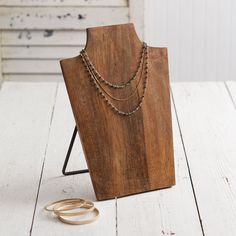 a wooden stand holding two necklaces on it's sides and a pair of gold rings next to it