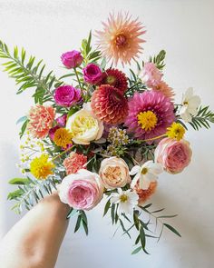 a bouquet of flowers is being held up by someone's hand in front of a white wall