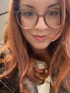 a close up of a person wearing glasses with long red hair and brown eyeglasses