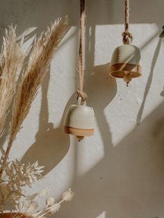 three ceramic bell ornaments hanging from twine with dried grass in the foreground and sunlight streaming through them