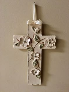 a white cross with flowers on it hanging from the side of a wall in a room