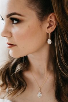 a woman with long hair wearing a white dress and gold earrings, looking off to the side