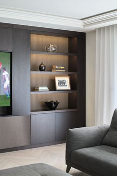 a living room with a gray couch and bookcase next to a white curtained window