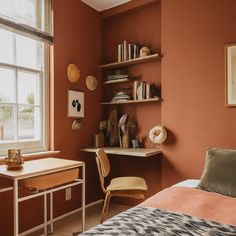 a bedroom with orange walls and a desk in front of a window that has bookshelves on it