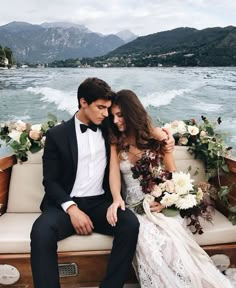 a man and woman sitting on a boat in front of the water with flowers around them