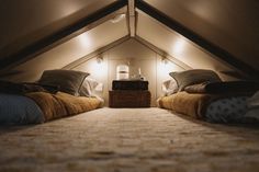 two beds with blankets and pillows in an attic bedroom under the roof light bulbs are turned on