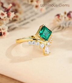 an emerald colored ring with white stones on top and gold band around the band, sitting on a piece of paper