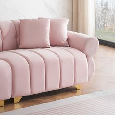 a pink couch sitting on top of a hard wood floor next to a large window