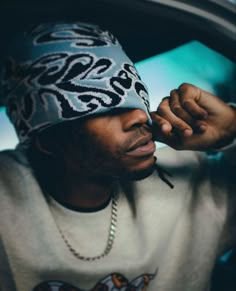 a man wearing a beanie and holding his hand up to his face while sitting in the back seat of a car