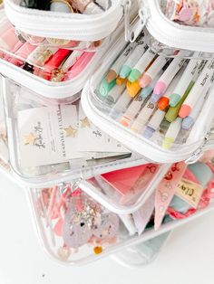 several clear containers filled with different types of pens and markers on top of each other