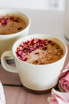 two white cups filled with hot chocolate and pink flowers