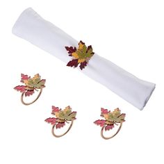 three napkin rings with leaves on them sitting next to a white napkin and two napkin holders