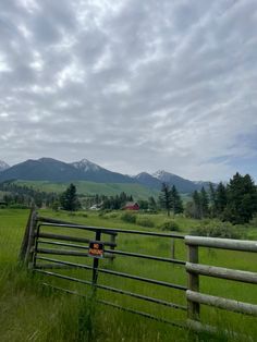 a wooden fence in the middle of a grassy field with mountains in the back ground