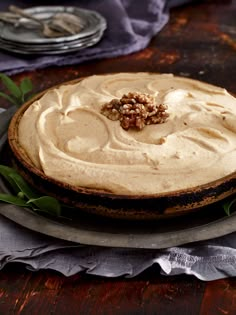 a cake with white frosting and walnuts on top sits on a plate next to silverware