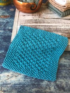 a blue knitted dishcloth sitting on top of a wooden table next to a copper bowl