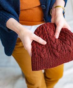 a woman holding a red knitted heart in her right hand and wearing brown pants