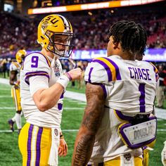 two football players standing next to each other on a field with fans in the background