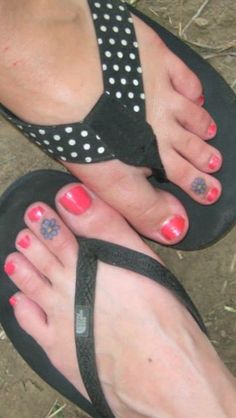 a person with red and white nail polish on their feet wearing flip flops in the dirt