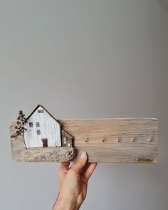 a person holding up a piece of wood with a house on it