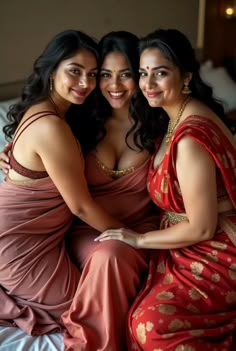 three beautiful women sitting next to each other on top of a bed in red dresses