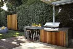 an outdoor kitchen with two bar stools next to it and a bbq grill