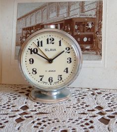 an alarm clock sitting on top of a doily next to a picture with a train in the background