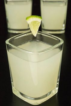 two shot glasses filled with white liquid and lime wedged into the glass, on a black surface